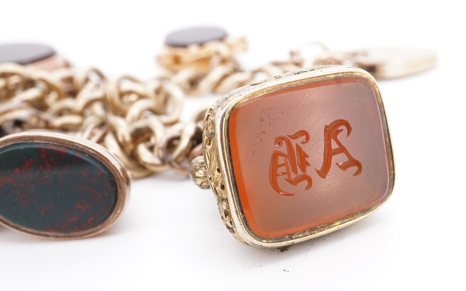 A 1970's 9ct gold curb link charm bracelet, with 9ct gold heart shaped clasp, hung with seven assorted gold or gilt metal mounted charms including six chalcedony set fob seals, gross weight 73 grams.